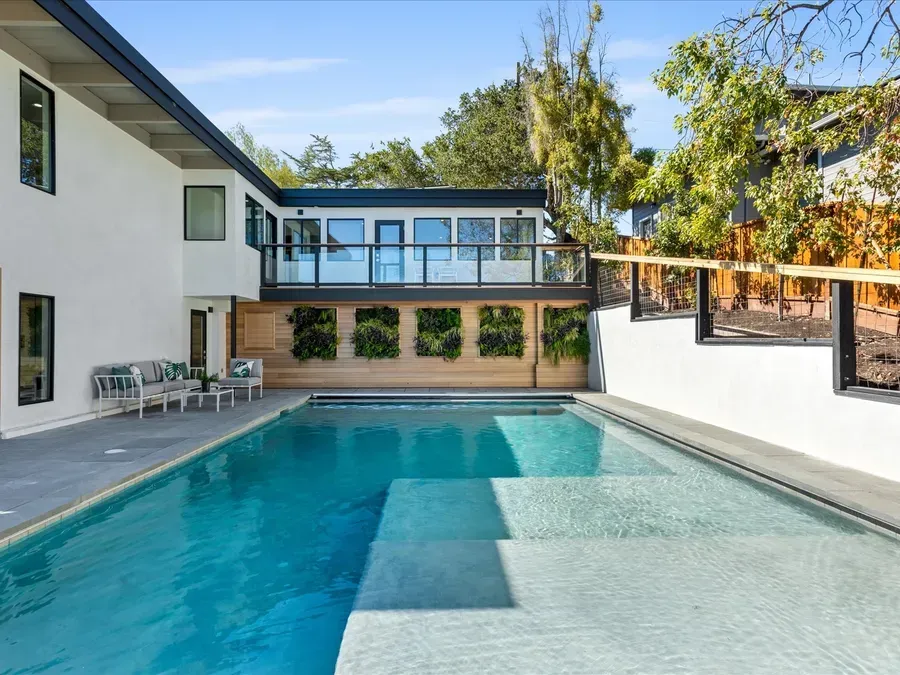 Modern house with pool, two-story structure, living wall, and upper-level balcony with glass railings.