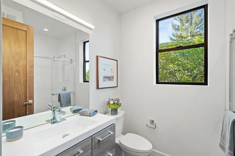 Bathroom with white walls, grey vanity, and a window overlooking greenery.