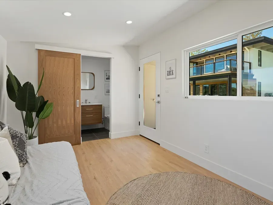 Bright room with wood floors, a sliding door to a bathroom, door to the outside, and a window with a view.