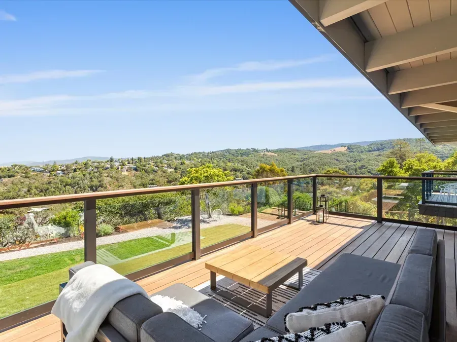 Deck with outdoor furniture overlooking a green, hilly landscape on a sunny day.