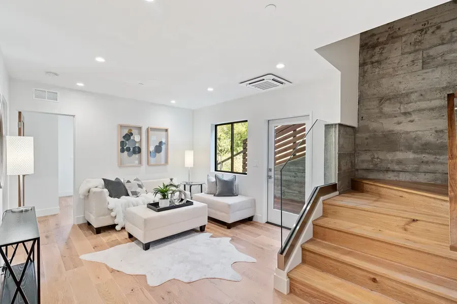 Living room with light wood floors, white walls, and stairs leading up.