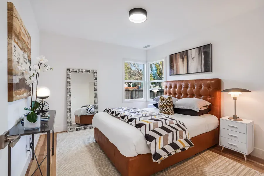 Bedroom with brown leather bed, white walls, large mirror, and decorative accents.