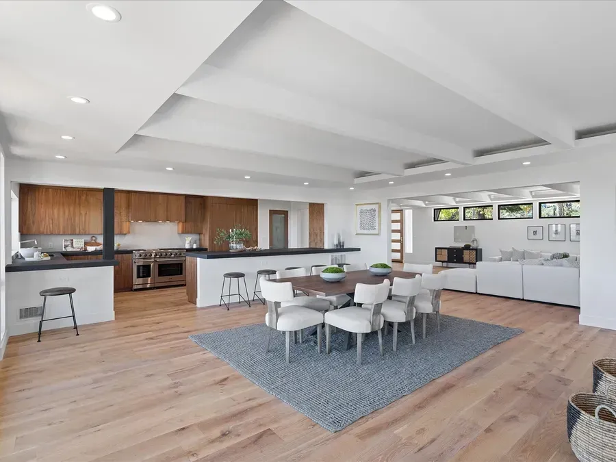 Open-plan kitchen, dining, and living area with hardwood floors, white walls, and wooden cabinets.