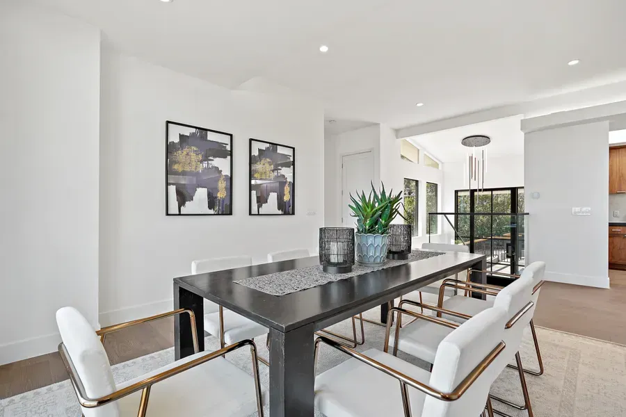 Dining room with a dark rectangular table, white chairs, artwork, and a potted plant.
