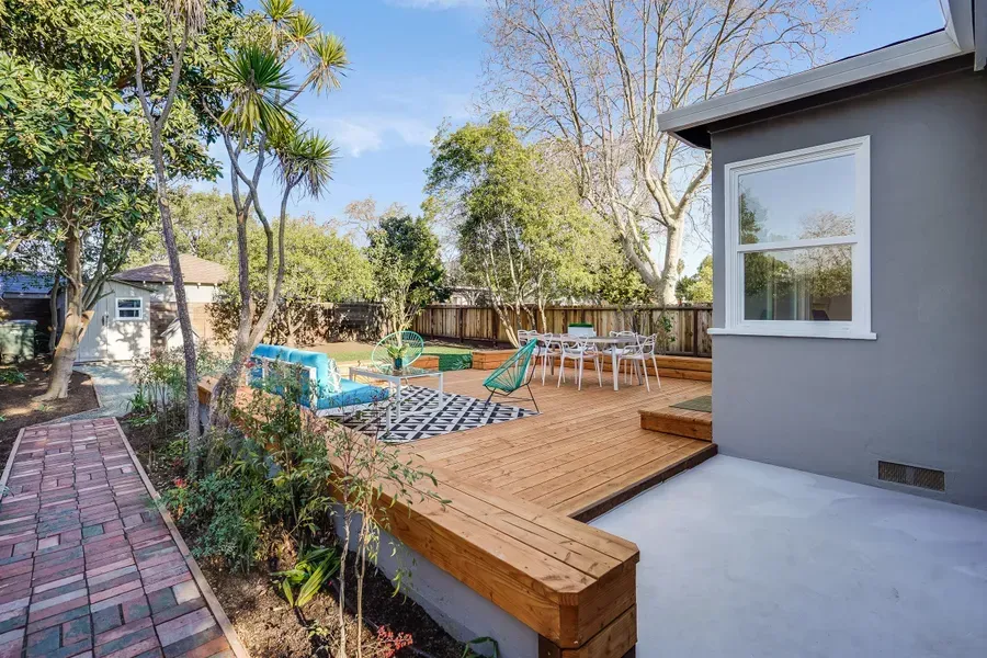 Wooden deck and patio with outdoor furniture, trees, and brick pathway.