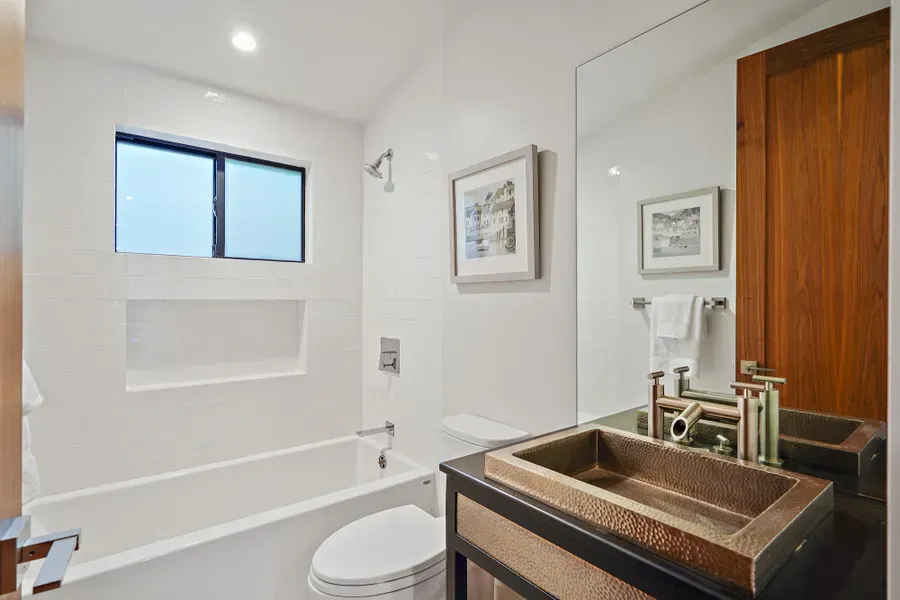 Modern bathroom with white walls, a copper sink, and wooden accents.