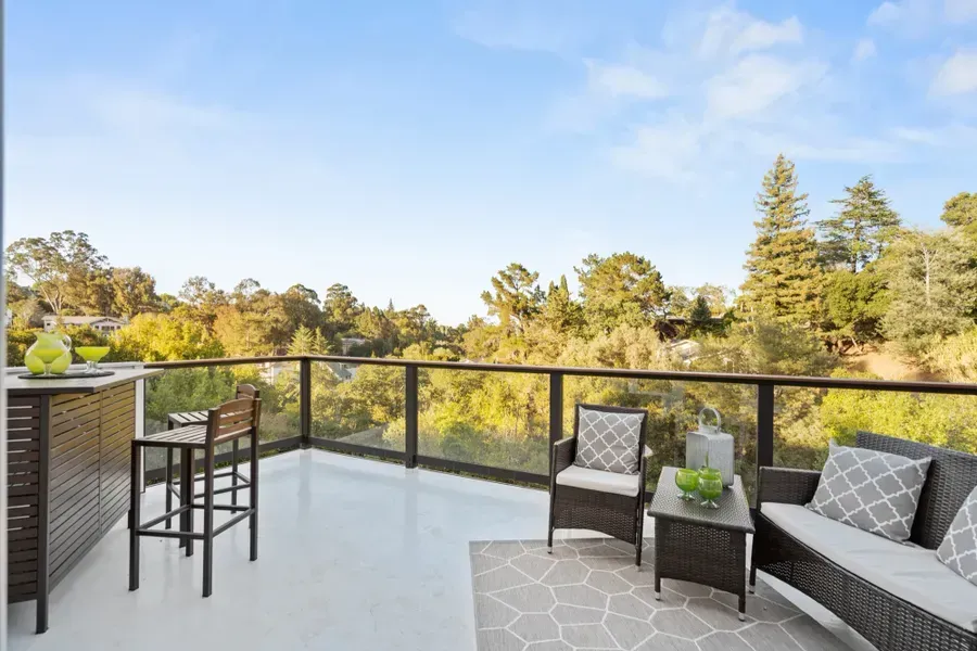 Patio with seating, bar, and glass railing overlooking trees and a blue sky.