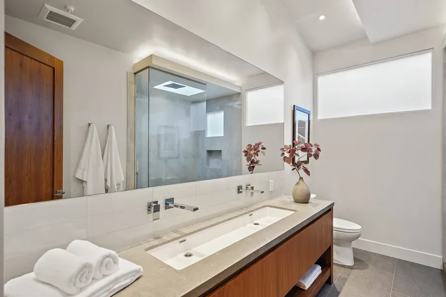 Modern bathroom with double sink vanity, large mirror, walk-in shower, and toilet.