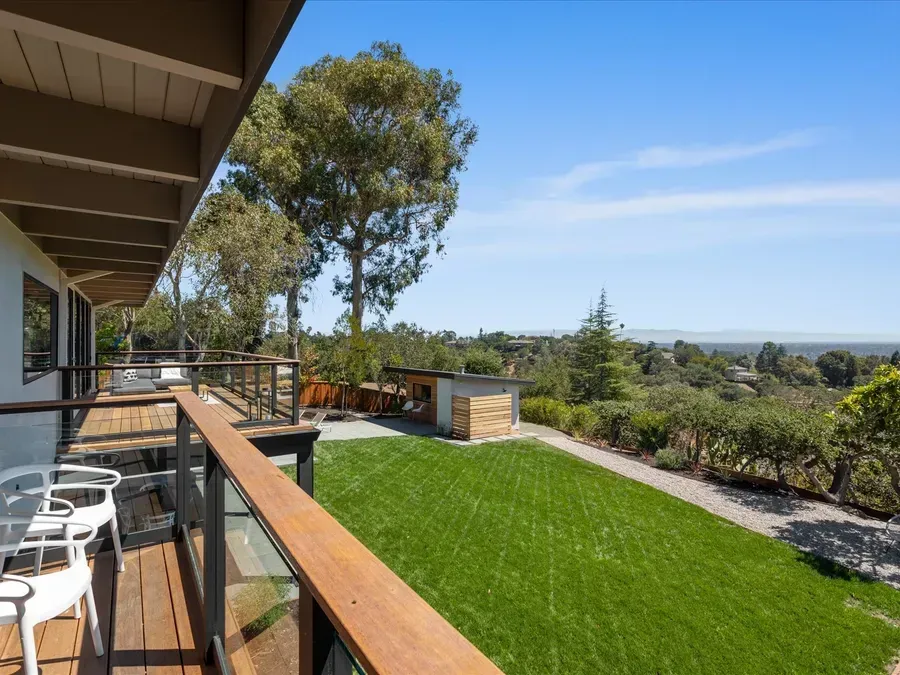 Backyard view with deck, green lawn, trees, and partial view of a cityscape under a blue sky.