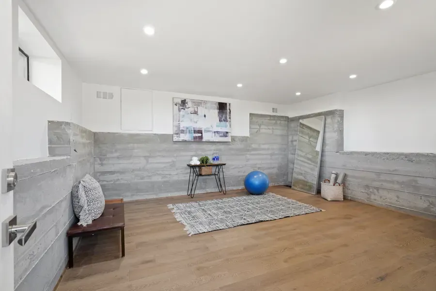 Basement yoga room: Concrete walls, hardwood floor, blue exercise ball, mirror, rug, artwork.