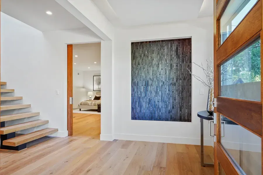 Entryway with hardwood floors, stairs, and modern art on a white wall. Wooden door and open doorway to a bedroom.