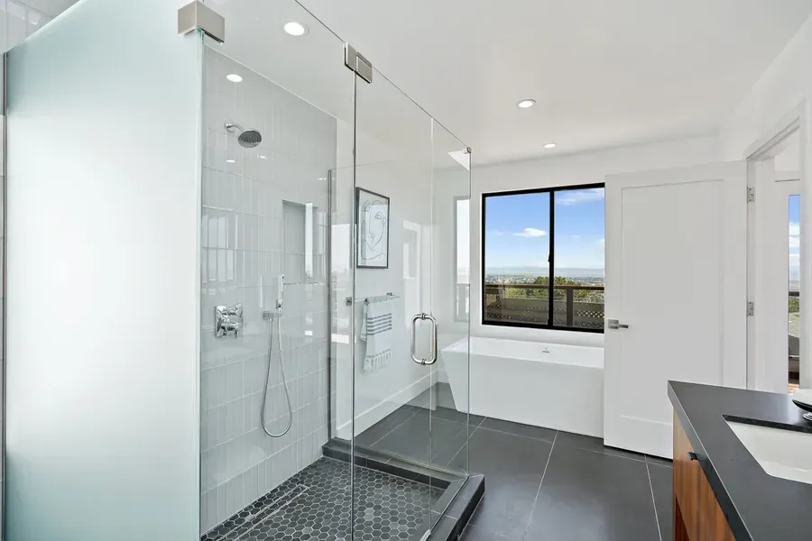 Modern bathroom with a glass shower, soaking tub, and window overlooking a view.