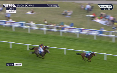 Horses racing at Epsom Downs. Jockey in blue leads, followed by another in green. Green grass and white fences.