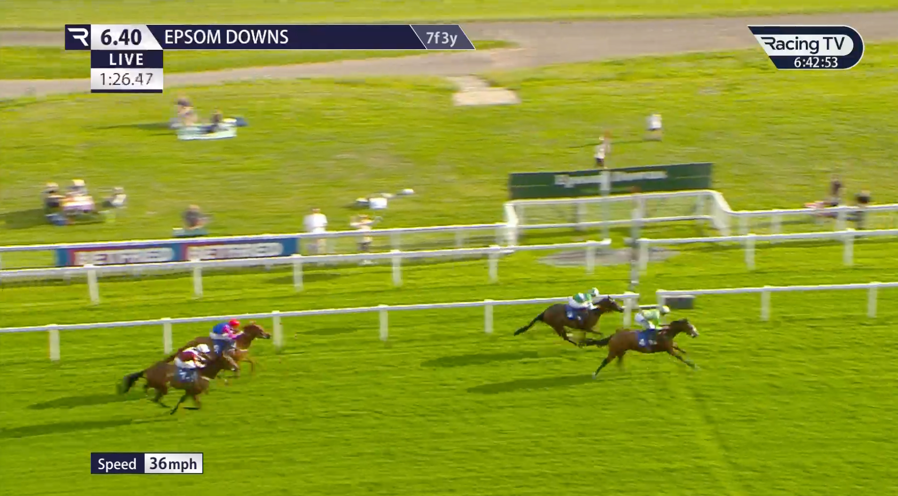 Horses racing on a grassy track at Epsom Downs, jockeys in colorful silks nearing the finish line.
