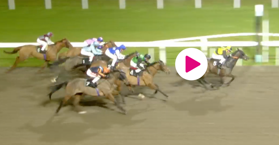 Horses racing on a track at night, jockeys on their backs.