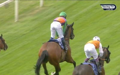 Two jockeys riding brown horses on a grassy race track. One wears green, the other orange, racing side-by-side.