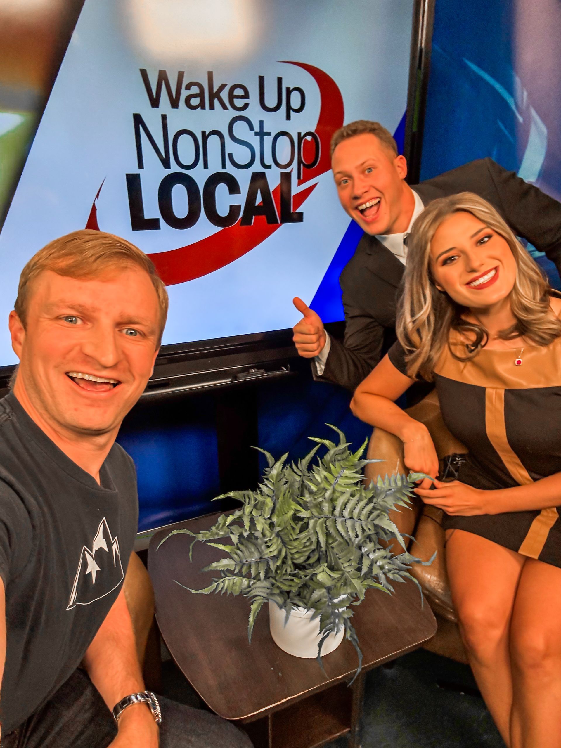 Three people are posing for a picture in front of a sign that says wake up nonstop local
