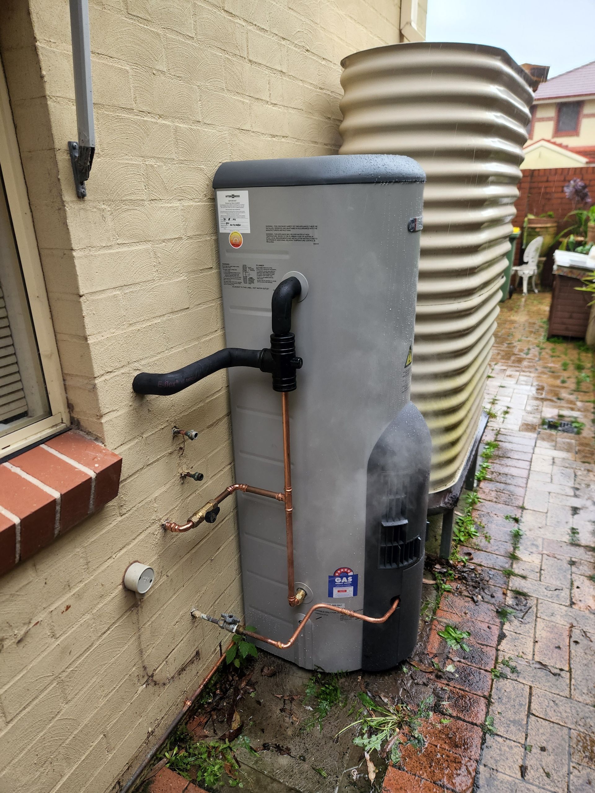 A White Water Heater is Sitting Next to a White Tank in a Room — Solar Services in Erina, NSW