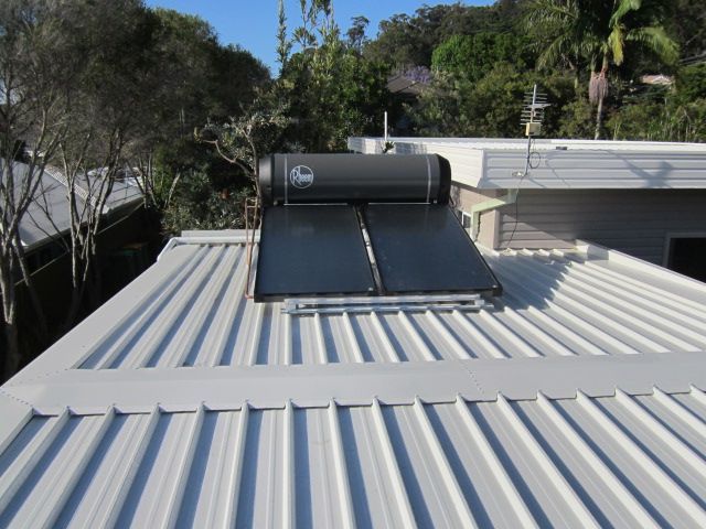 Rheem solar hot water heater mounted on a white corrugated metal roof with trees in the background — Solar Services in Erina, NSW