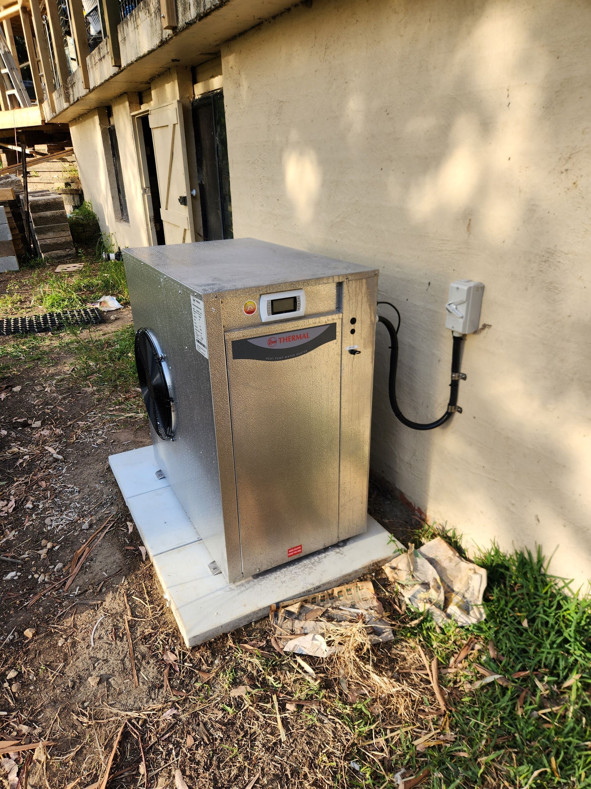 Metal HVAC unit on a concrete pad next to a building wall and electrical box  — Solar Services in Erina, NSW