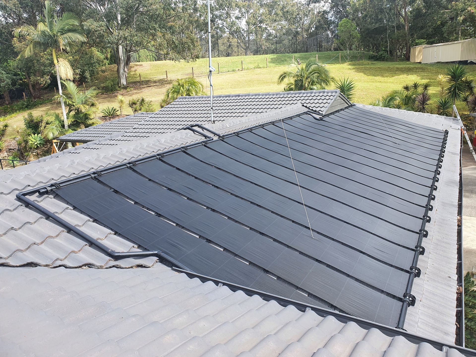 Dark gray metal roof panels installed on a house, viewed from above with trees and lawn in the background — Solar Services in Erina, NSW