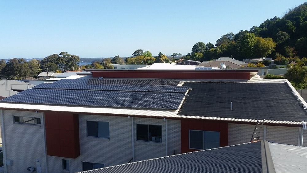 Residential Rooftops With Solar Panels Under A Clear Blue Sky — Solar Services in Erina, NSW