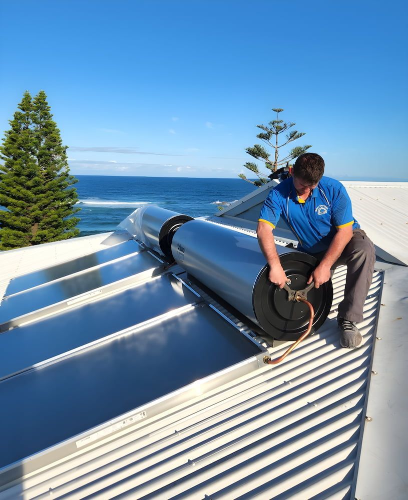 A Man is Sitting on a Roof Working on a Solar Water Heater — Solar Services in Gosford, NSW