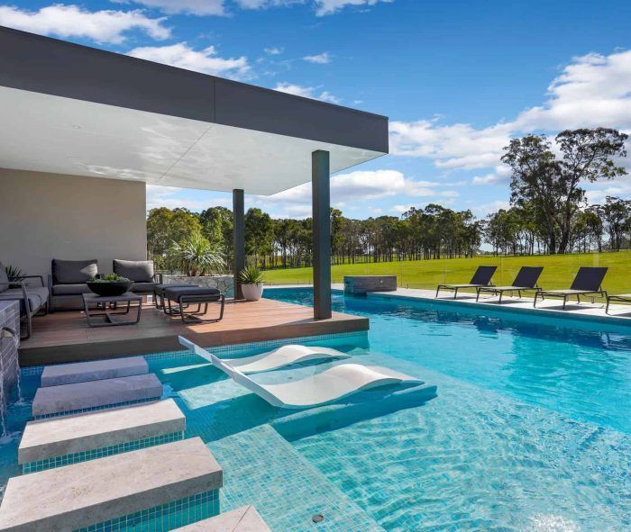 Luxurious pool with lounge chairs, covered seating area, and green landscape under a blue sky  — Solar Services in Erina, NSW