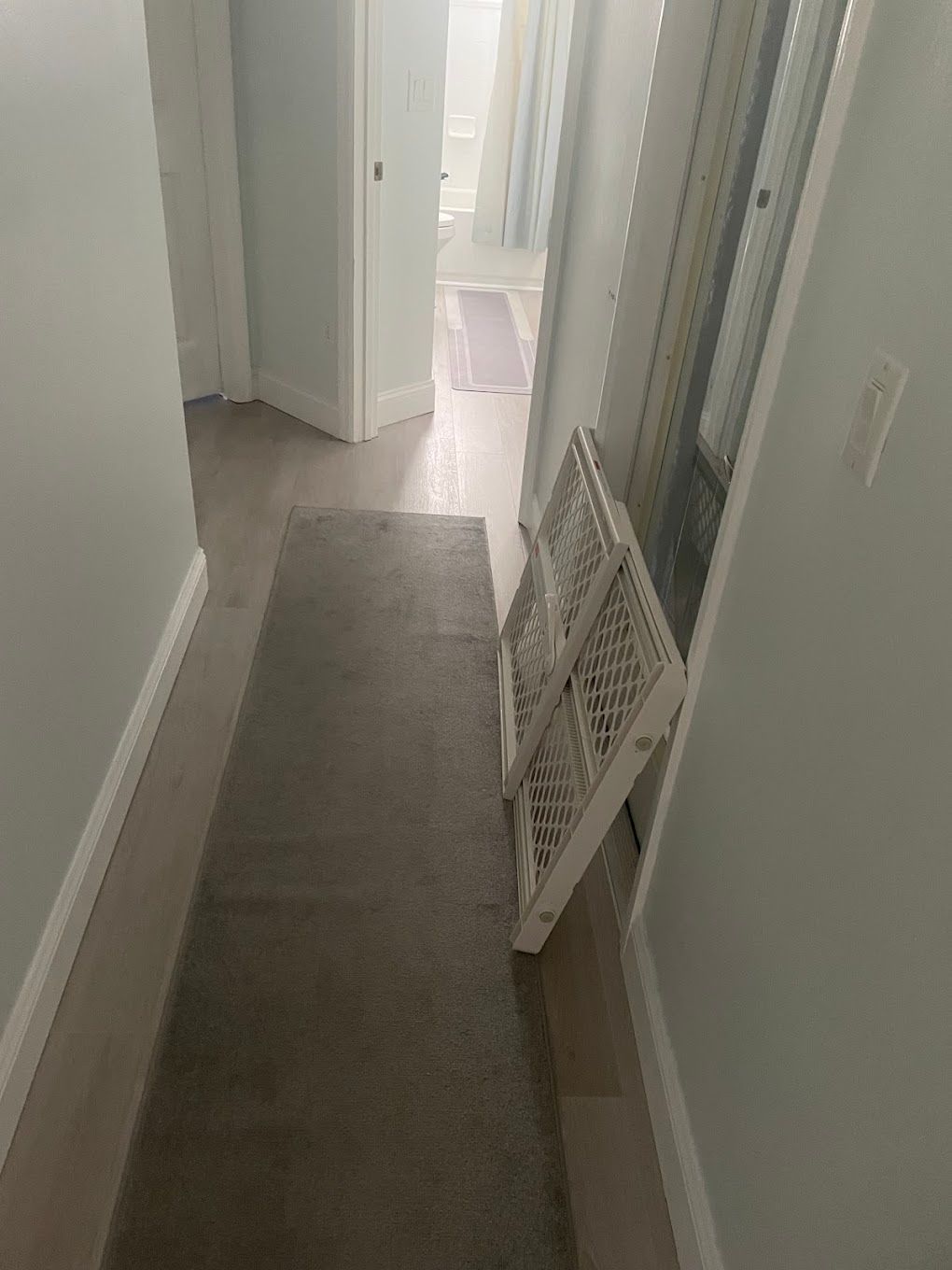Long hallway with gray rug and a white gate. Light blue walls and wood floor.