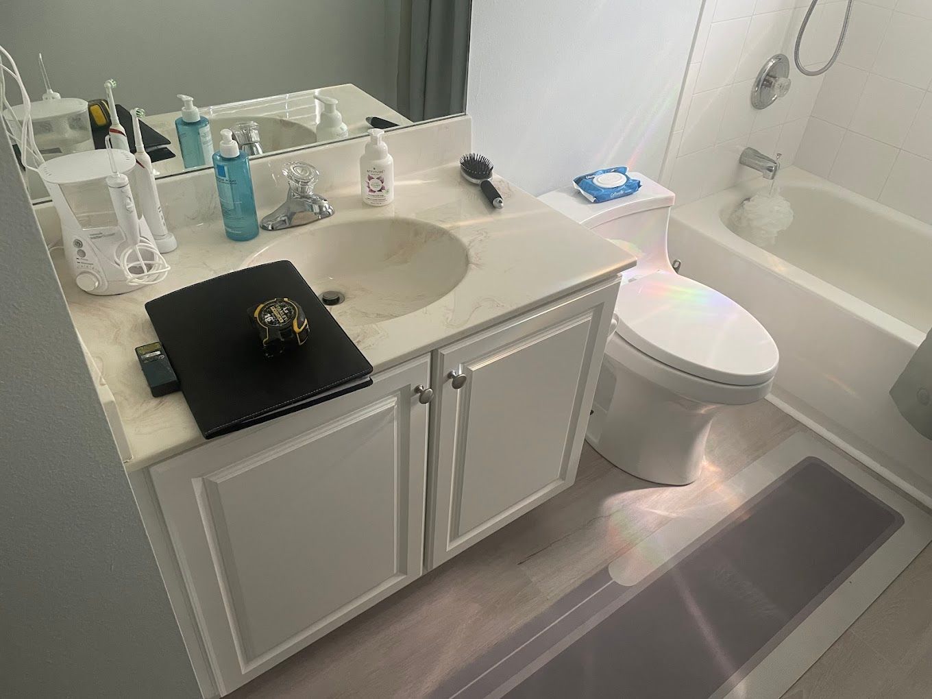 Bathroom with white vanity, sink, toilet, and bathtub; laptop on the counter.