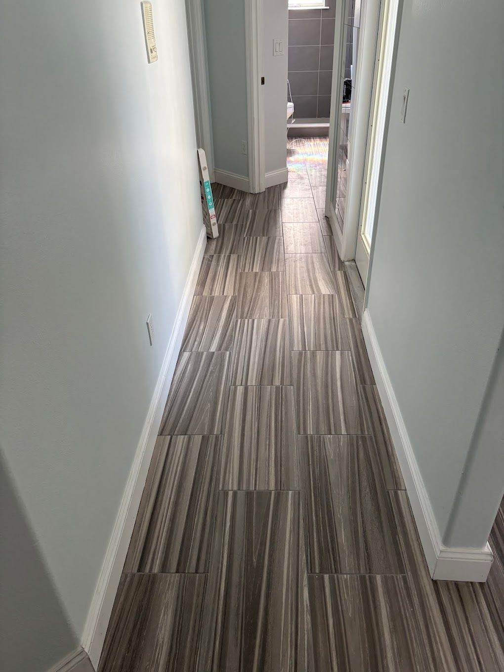 Narrow hallway with wood-look tile flooring, light blue walls, and a doorway at the end.