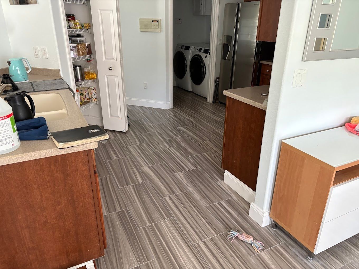 Kitchen interior with wood-look tile floor, cabinets, pantry, and laundry appliances in the background.