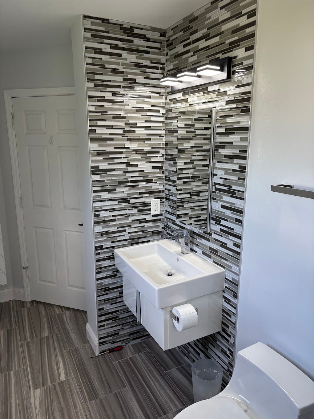 Small modern bathroom with floating sink, toilet, and patterned tile wall.