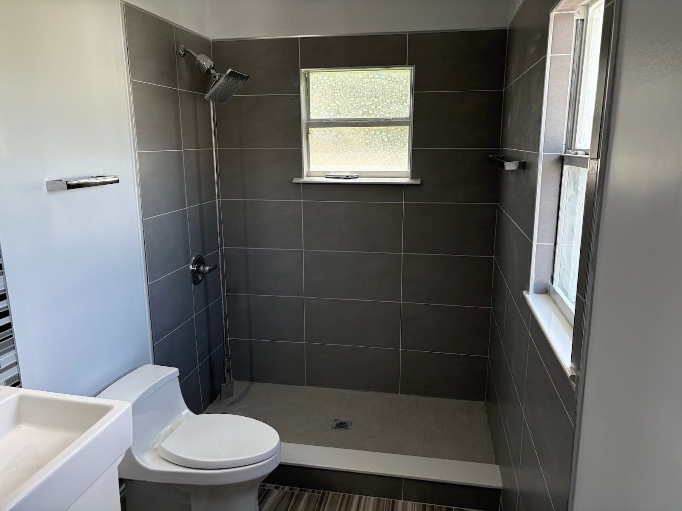 Bathroom with gray tile shower, toilet, window, and sink.