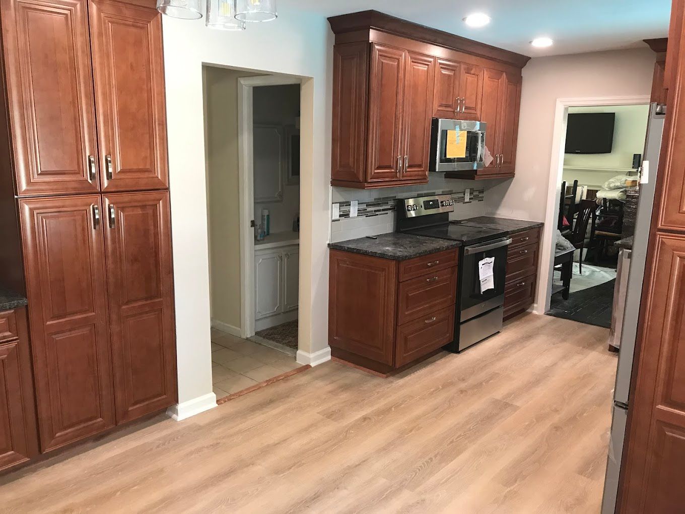 A kitchen with brown cabinets, stainless steel appliances, light-colored floor, and a doorway to another room.