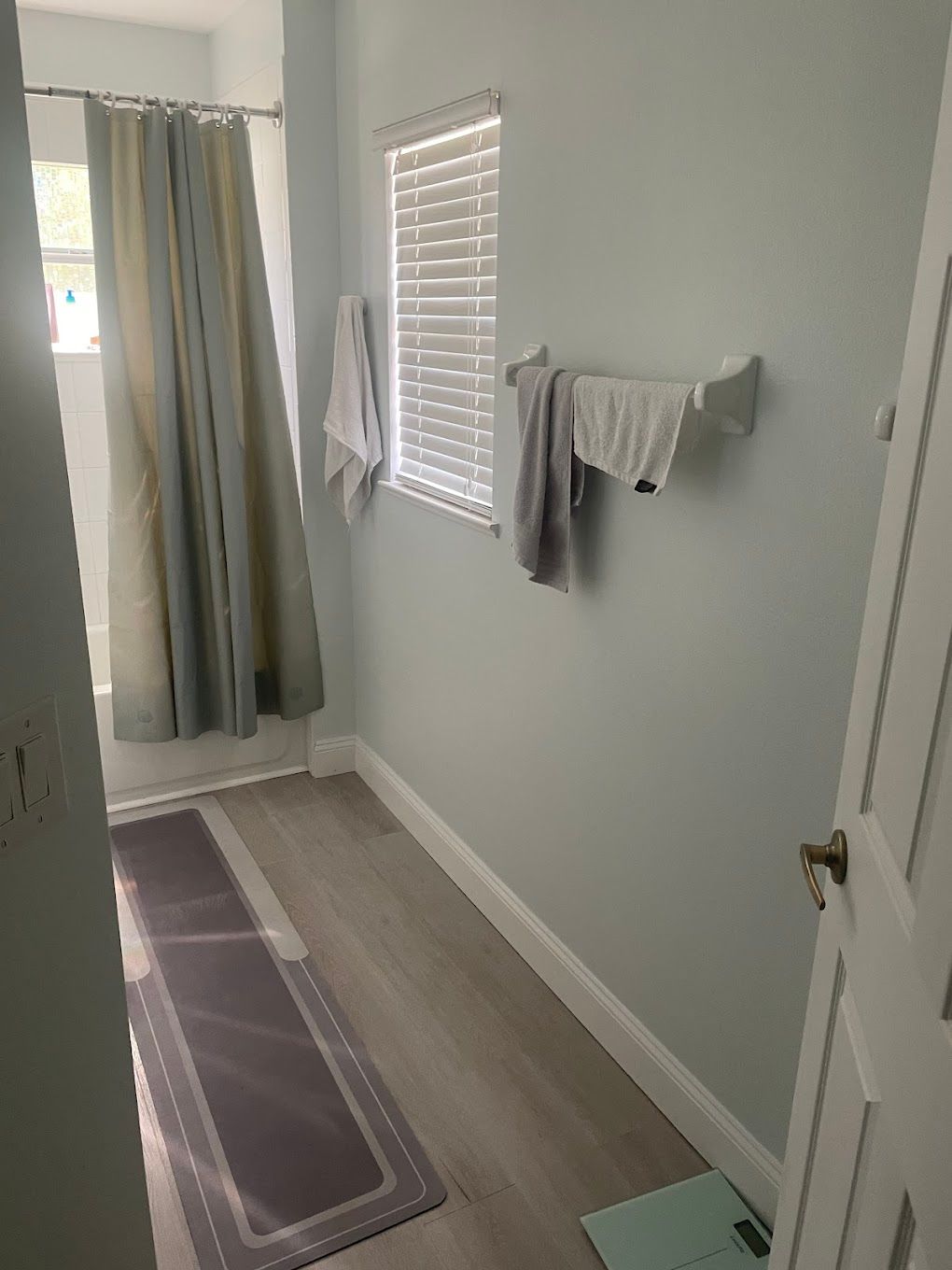 Small bathroom with light blue walls, a shower with a curtain, a window, and a towel rack.