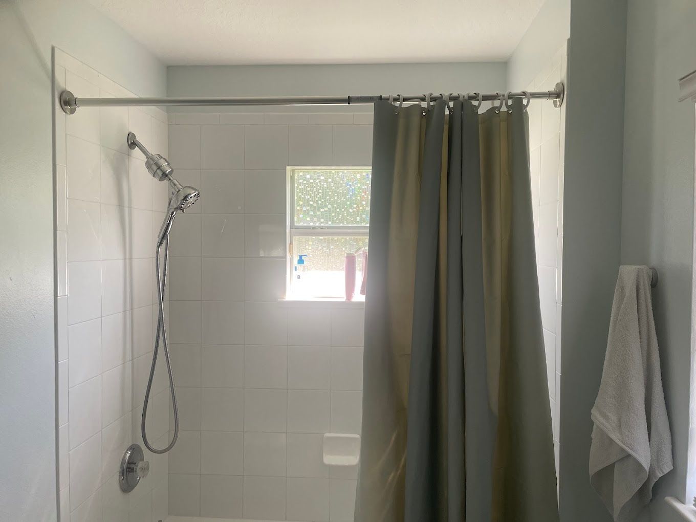 Shower with white tile, shower curtain, and towel hanging on the wall.