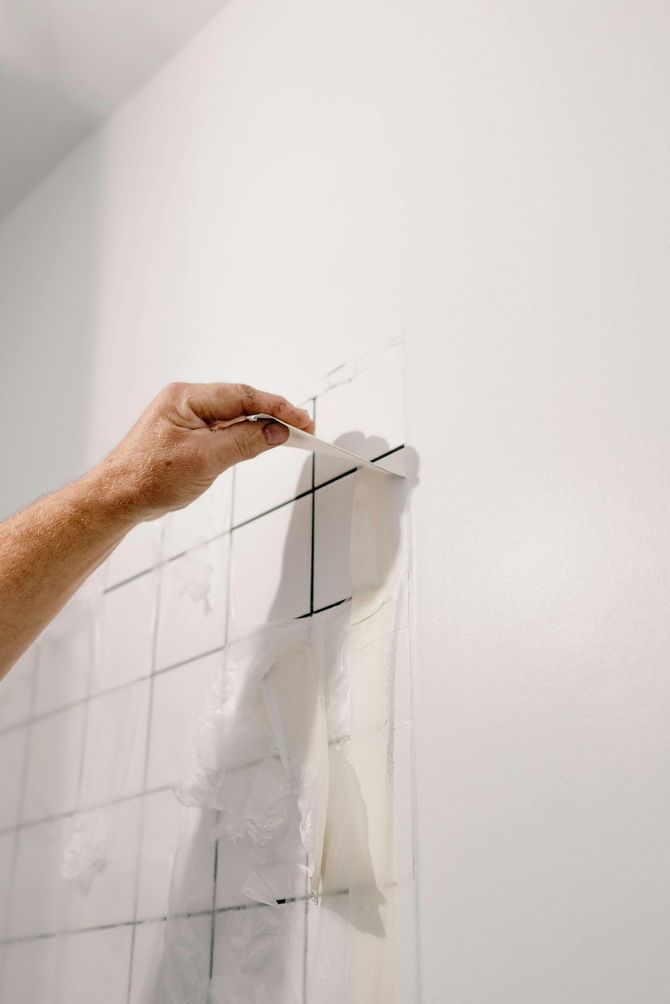 A person is cutting tiles on a wall with a pair of scissors.