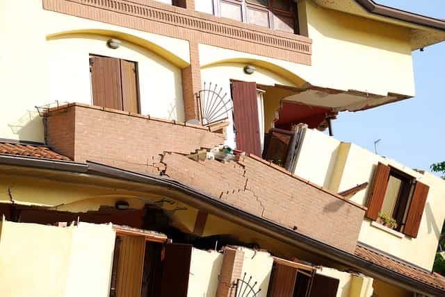 Collapsed multi-story building with broken walls, leaning balcony, and shattered windows