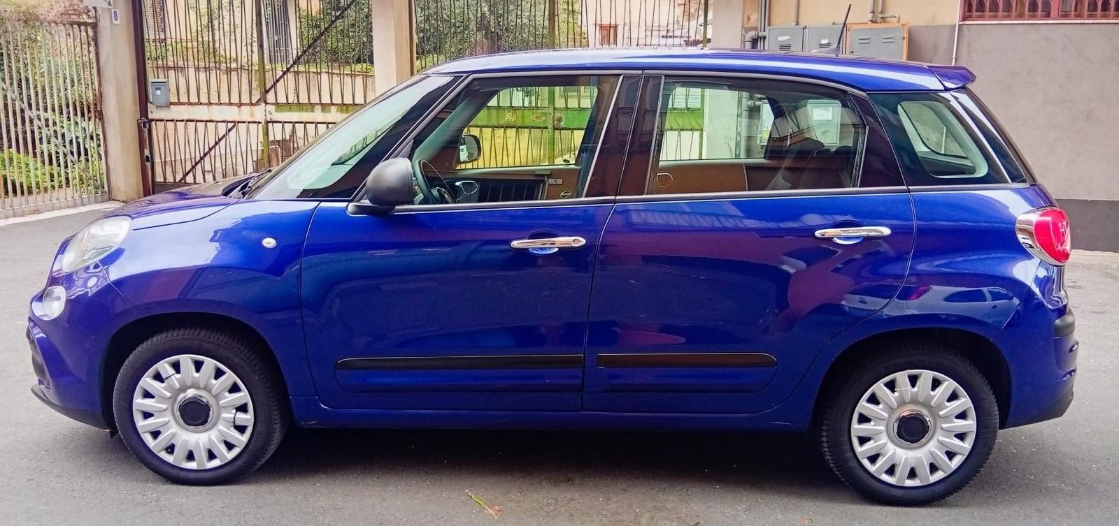 Fiat 500L blu parcheggiata in strada. Ha cerchi bianchi e vetri oscurati.