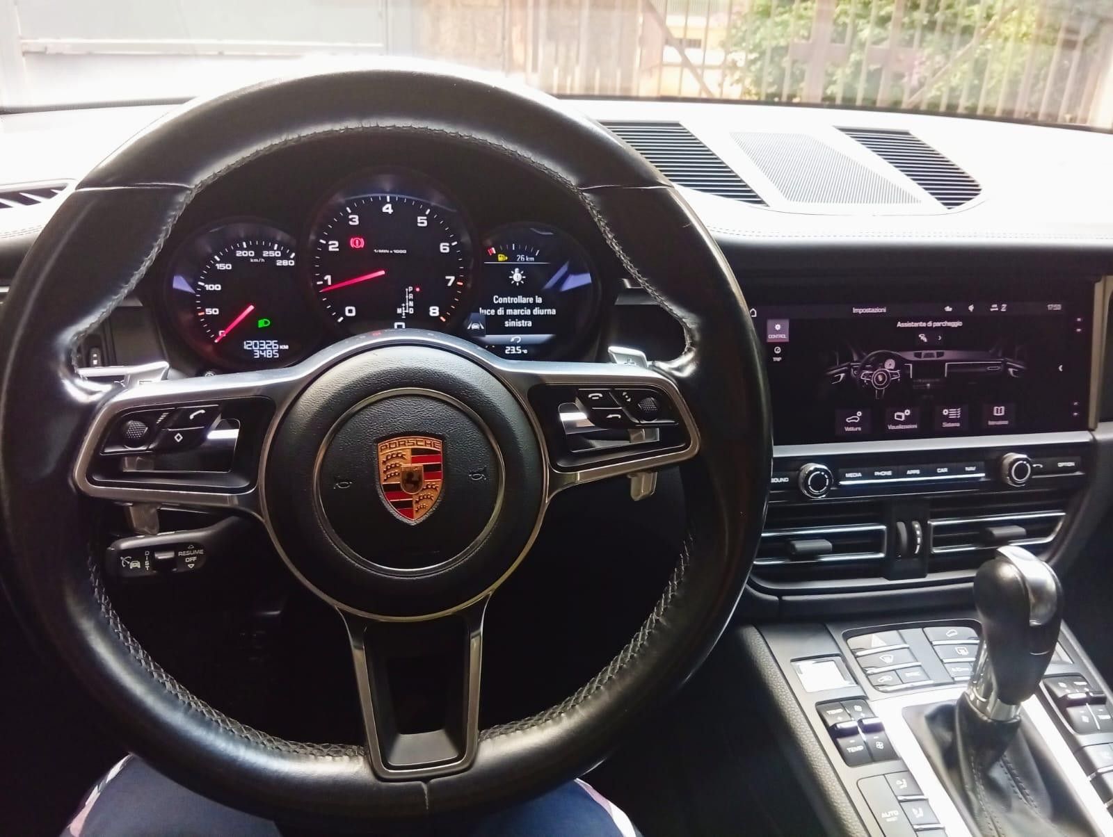 Vista interna del cruscotto di un'auto Porsche con volante, indicatori e schermo di infotainment.
