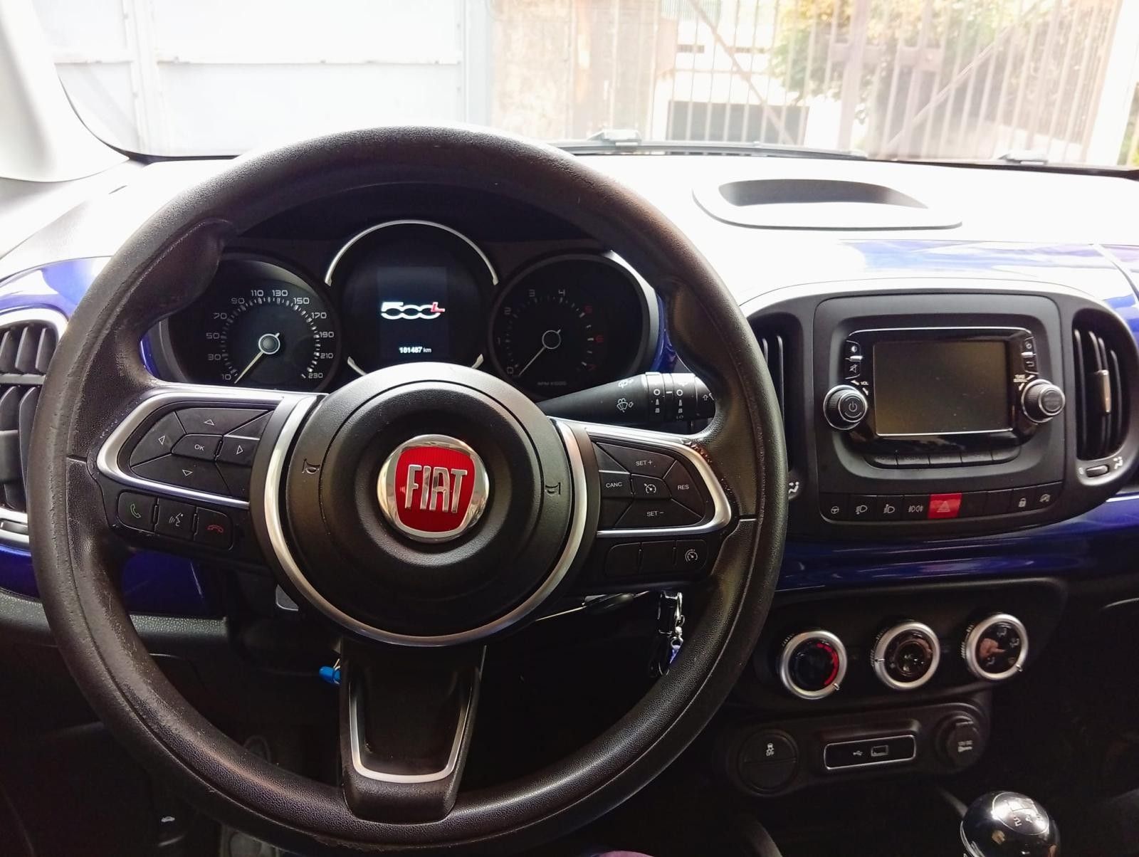 Cruscotto di una Fiat 500L blu, volante con logo Fiat, indicatori e schermo dell'infotainment visibili.
