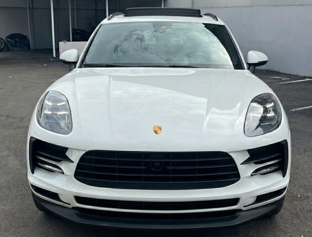 SUV Porsche Macan bianco con griglia nera, parcheggiato davanti a un edificio.