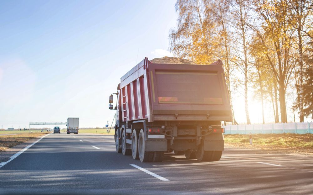 Dump Truck Driving on a Sunny Road, With a Second Truck in the Distance, Trees, and Blue Sky — Hasti Skips in Bangalow, NSW
