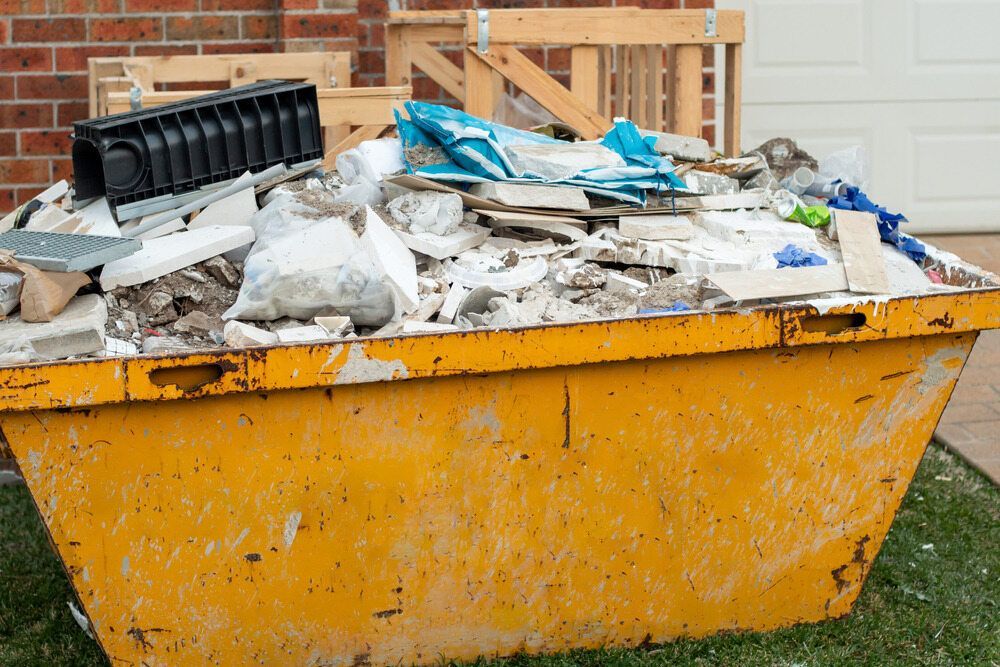 Yellow Dumpster Overflowing With Construction Debris in Front of a Brick House — Hasti Skips in Bangalow, NSW