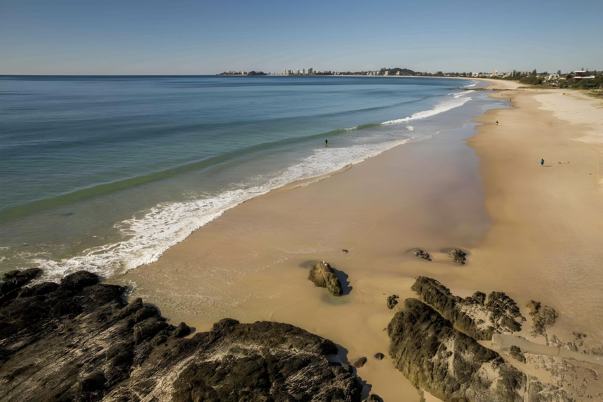 Sandy Beach With Gentle Waves Under a Clear Blue Sky, With Rocks in the Foreground — Hasti Skips in Tweed Heads, NSW