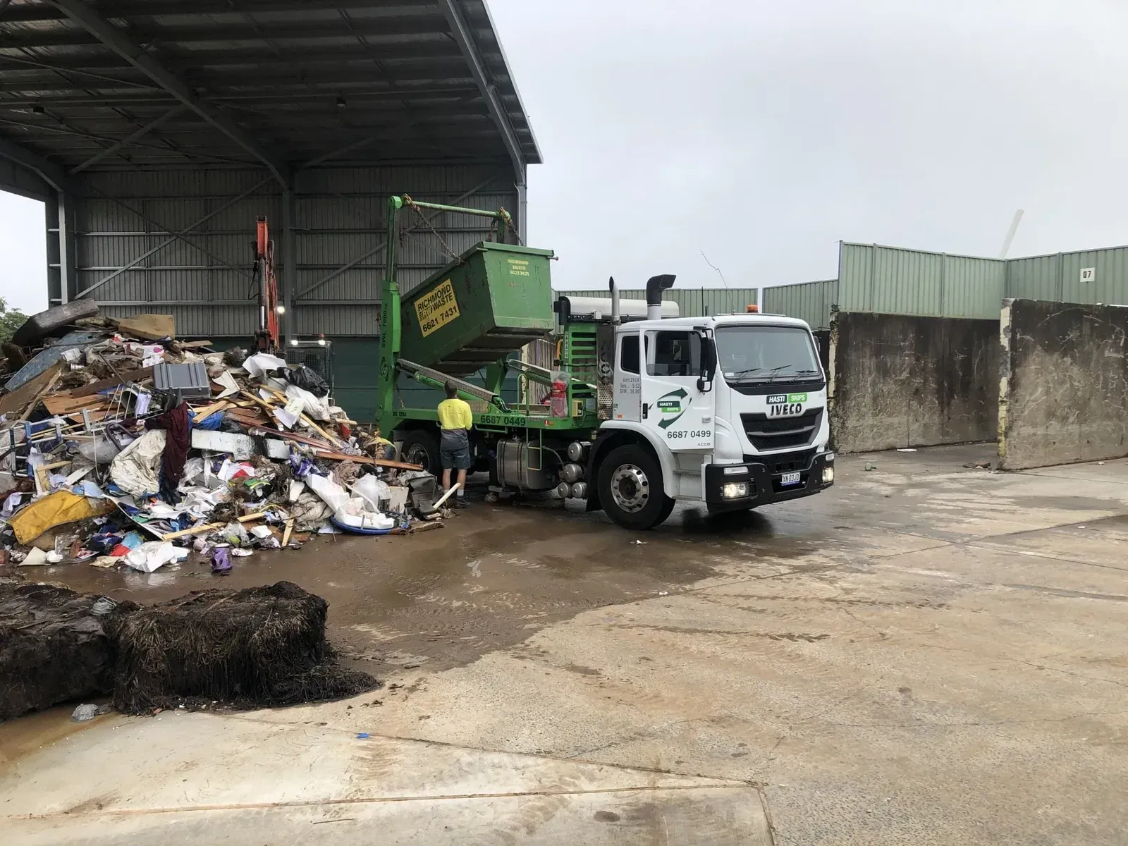 A Recycling Truck Empties a Green Waste Bin at a Facility a Worker Stands Nearby — Hasti Skips in Bangalow, NSW