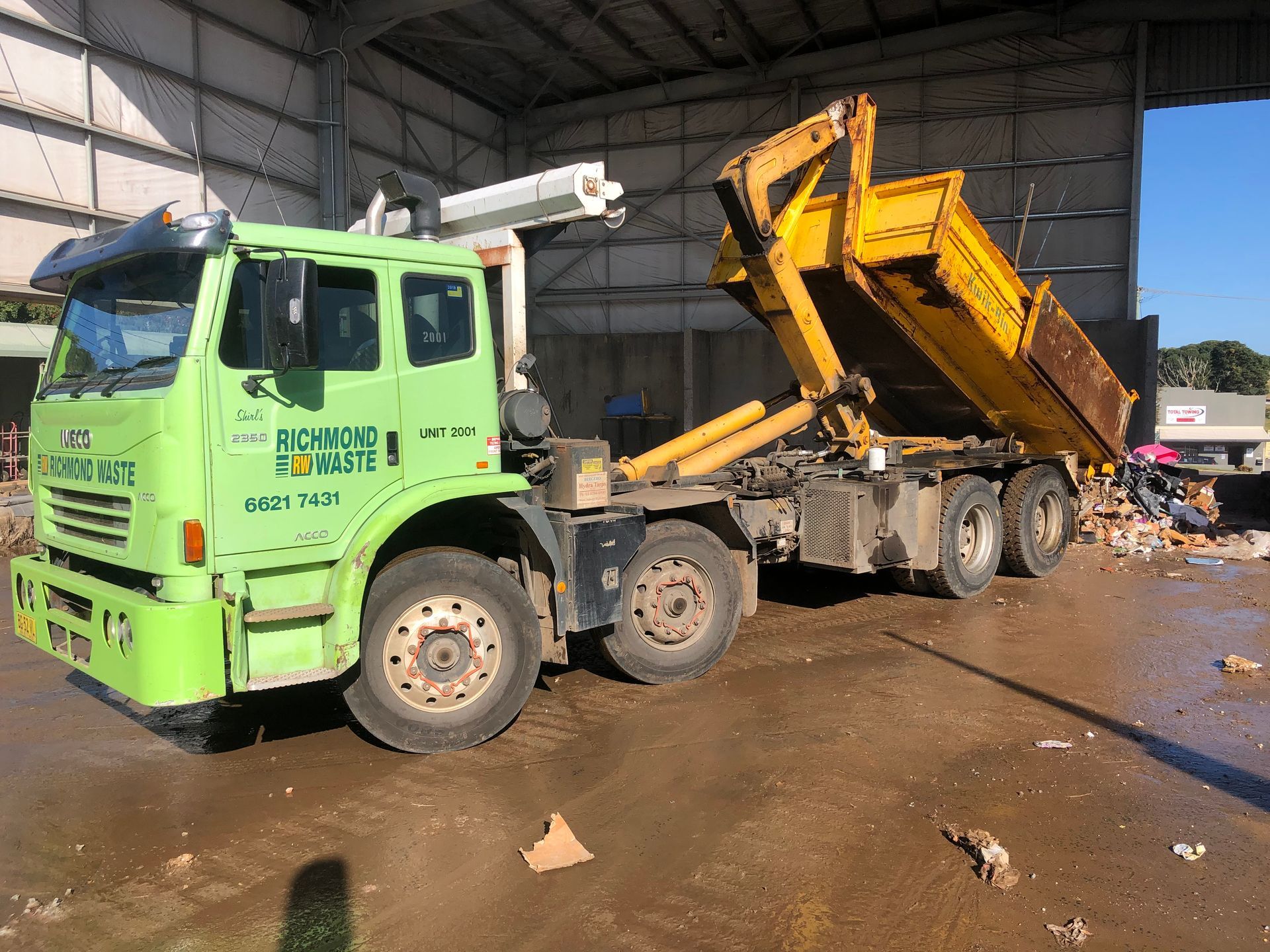 A large green richmond waste truck is parked by a rubiish dump building — Hasti Skips in Bangalow, NSW