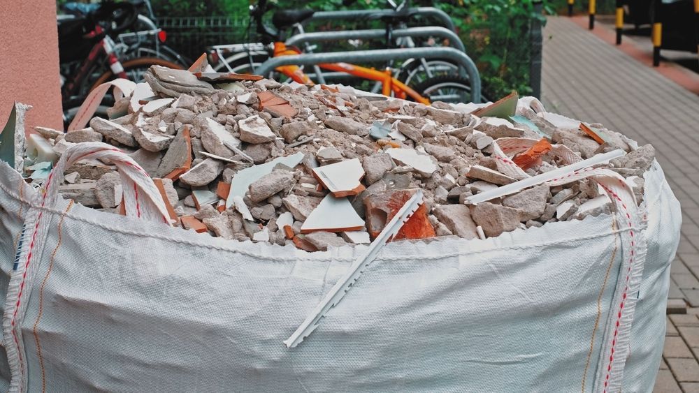 Large White Bag Filled With Rubble and Debris, in Front of Bicycles on a Brick Sidewalk — Hasti Skips in Bangalow, NSW