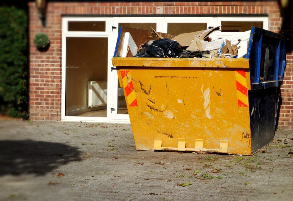 Yellow Dumpster Overflowing With Debris in Front of a Brick Building With Open Glass Doors — Hasti Skips in Evans Head, NSW